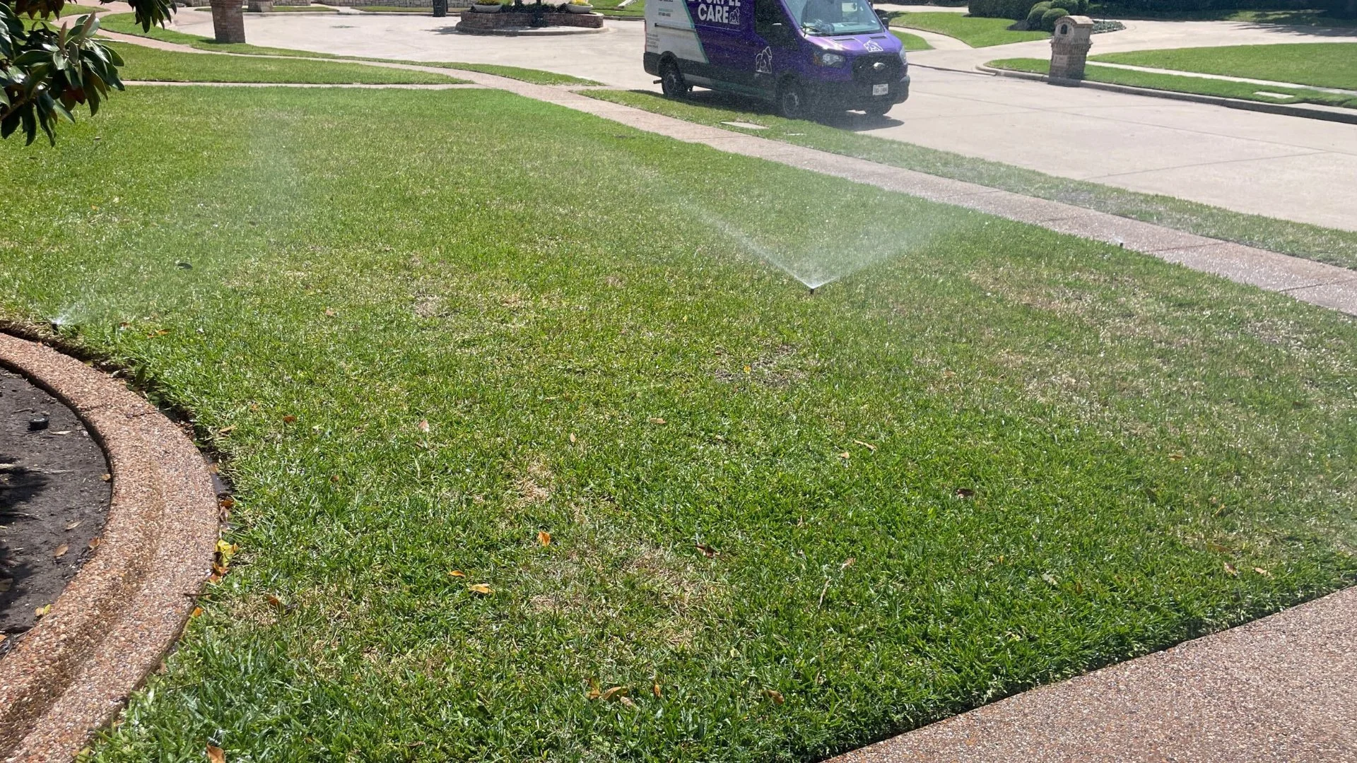 Well-maintained lawn being watered by a sprinkler, with a service van in the background, highlighting lawn care services.
