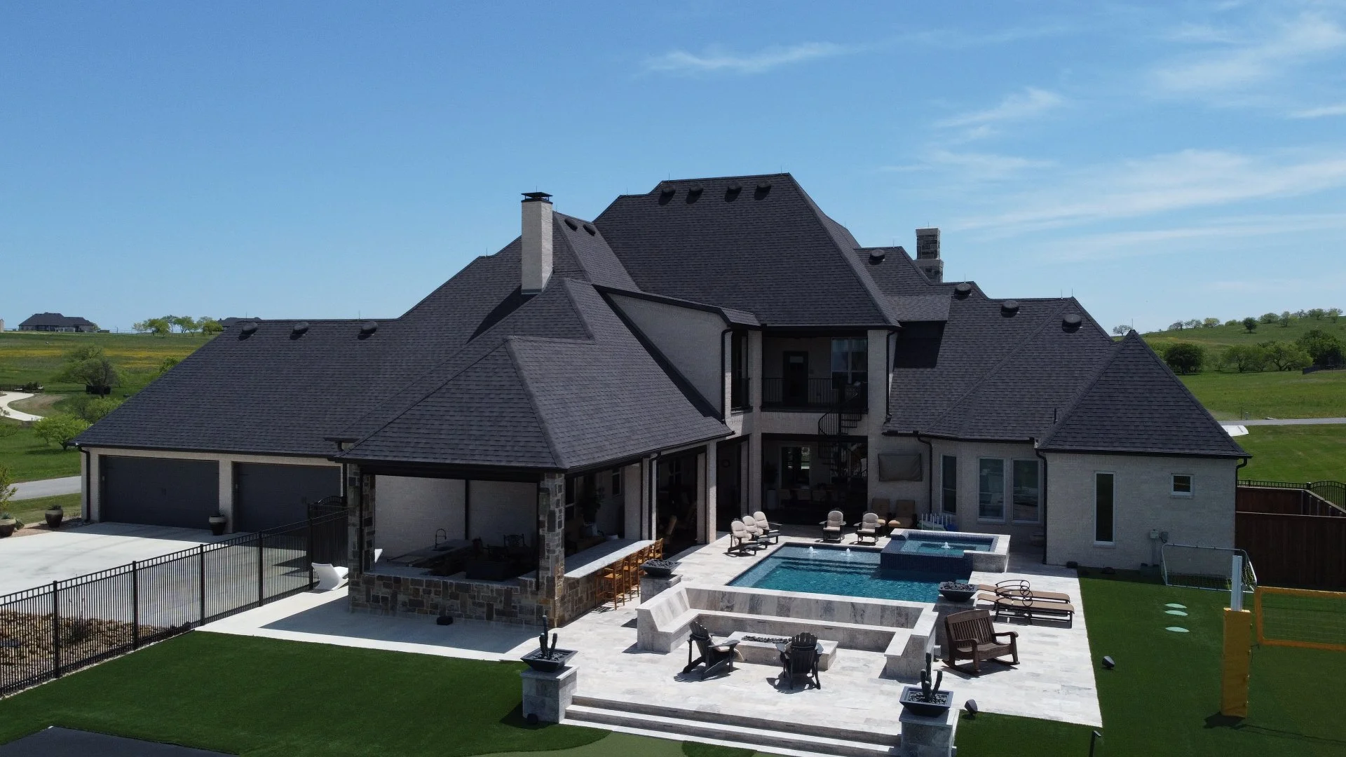 Aerial view of a luxury home featuring a spacious backyard with a swimming pool, elegant patio, and landscaped areas under a clear blue sky.