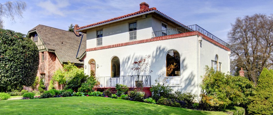 A charming home with a beautifully landscaped front yard, featuring a lush green lawn and colorful flower beds, framed by trees and a clear blue sky.