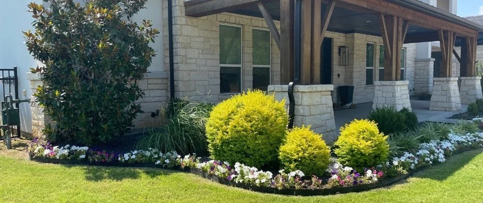 Beautifully landscaped front yard featuring lush greenery and colorful flower beds around a modern home with wooden porch.