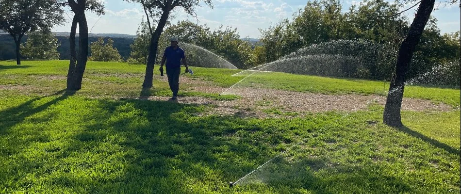 Sprinkler heads watering a lawn in Fort Worth, TX, near a worker.