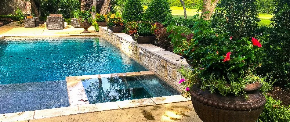 A serene poolside view featuring a sparkling blue pool surrounded by beautifully arranged potted plants and comfortable seating, framed by lush greenery.