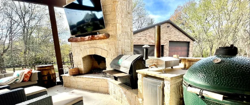 An inviting outdoor kitchen area featuring a stone fireplace and modern cooking appliances.