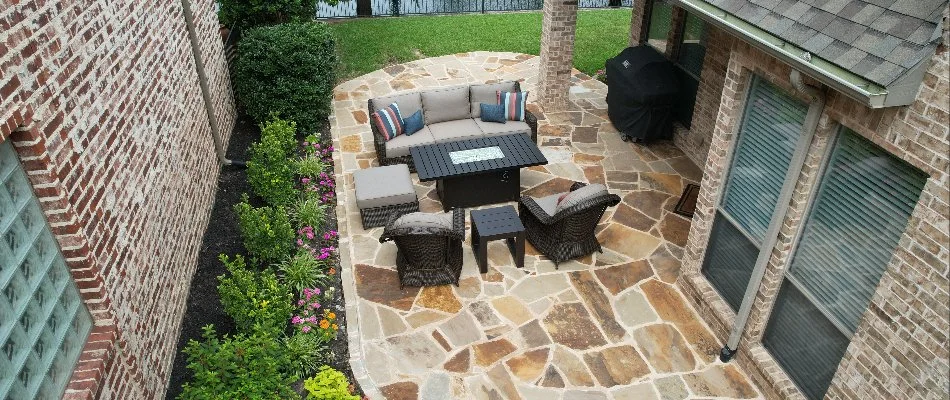 An inviting outdoor patio with a comfortable seating area, featuring stylish furniture and vibrant flower beds, set against a backdrop of a well-maintained yard and nearby water.