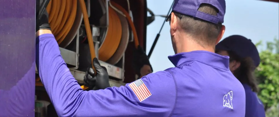 Worker in purple uniform operating equipment with yellow hoses in the background, showcasing hands-on service in a professional setting.