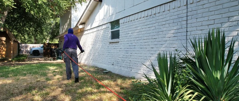 A worker applying a perimeter pest control treatment to a home in Fort Worth, TX.